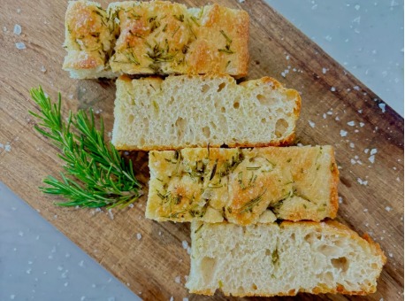 Slices of rosemary focaccia beside a sprig of fresh rosemary